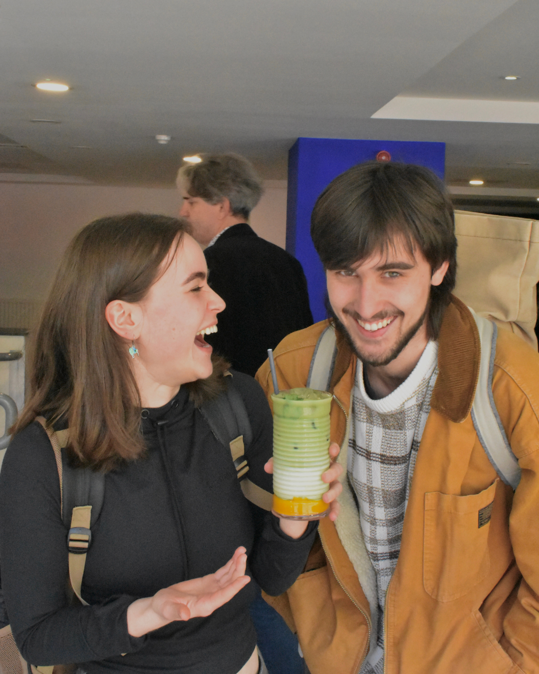 Two people laughing, with one holding a UAL matcha drink in hand. 