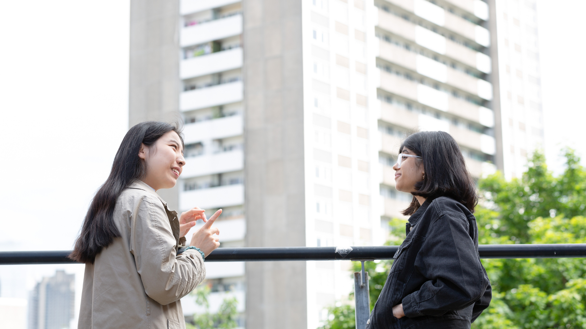 Two people standing on a terrace outside talking to each other.