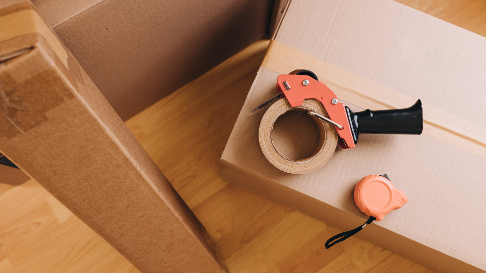 a cardboard box with a roll of tape and measuring tape on top